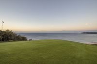 a beautiful view of the ocean and grass at dusk taken from an apartment overlooking the ocean