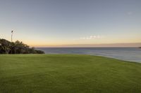 a beautiful view of the ocean and grass at dusk taken from an apartment overlooking the ocean