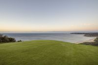 there is a green hill that overlooks the water's edge and beach at sunset