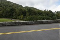 an empty road with stone retaininging on both sides and green hills in the background