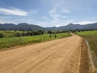 a dirt road with a grassy landscape next to it and mountains behind it with two tracks in the dirt