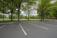 the empty parking lot of an apartment complex in front of a tennis court with many trees in the area