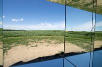 some large buildings reflecting in a mirror on the ground of a field with wind mills