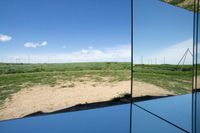 some large buildings reflecting in a mirror on the ground of a field with wind mills