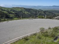 the paved road looks scenic with a lush green landscape around it with mountains in the distance