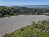 the paved road looks scenic with a lush green landscape around it with mountains in the distance