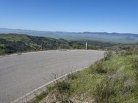 the paved road looks scenic with a lush green landscape around it with mountains in the distance