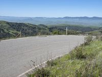 the paved road looks scenic with a lush green landscape around it with mountains in the distance