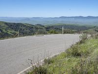 the paved road looks scenic with a lush green landscape around it with mountains in the distance