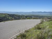 the paved road looks scenic with a lush green landscape around it with mountains in the distance