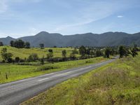 an empty rural road with a scenic view in the background of mountains and green fields