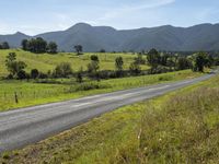 an empty rural road with a scenic view in the background of mountains and green fields