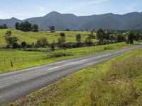 an empty rural road with a scenic view in the background of mountains and green fields