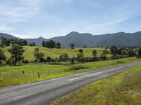 an empty rural road with a scenic view in the background of mountains and green fields