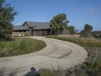 an old house is surrounded by lush green vegetation and a dirt road in front of it