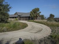 an old house is surrounded by lush green vegetation and a dirt road in front of it