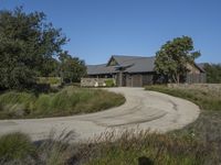 an old house is surrounded by lush green vegetation and a dirt road in front of it