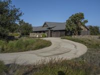 an old house is surrounded by lush green vegetation and a dirt road in front of it