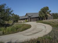 an old house is surrounded by lush green vegetation and a dirt road in front of it