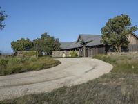 an old house is surrounded by lush green vegetation and a dirt road in front of it