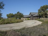 an old house is surrounded by lush green vegetation and a dirt road in front of it