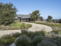 an old house is surrounded by lush green vegetation and a dirt road in front of it