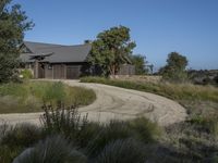 an old house is surrounded by lush green vegetation and a dirt road in front of it