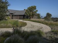 an old house is surrounded by lush green vegetation and a dirt road in front of it