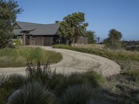 an old house is surrounded by lush green vegetation and a dirt road in front of it