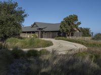 an old house is surrounded by lush green vegetation and a dirt road in front of it