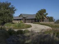 an old house is surrounded by lush green vegetation and a dirt road in front of it