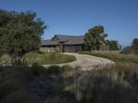 an old house is surrounded by lush green vegetation and a dirt road in front of it