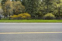 some trees in the background and a fence around one side of the road and a sign in front of it with yellow marking on it