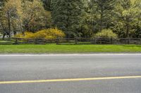 some trees in the background and a fence around one side of the road and a sign in front of it with yellow marking on it