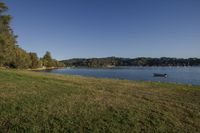 a view from the banks of a lake near the shore line of grass with boats in the distance