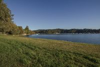 a view from the banks of a lake near the shore line of grass with boats in the distance