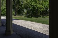 the view of a large open grassy park area from between two pillars with trees in background