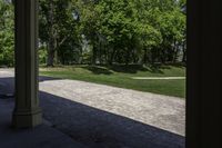 the view of a large open grassy park area from between two pillars with trees in background