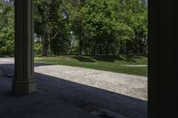 the view of a large open grassy park area from between two pillars with trees in background