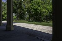 the view of a large open grassy park area from between two pillars with trees in background