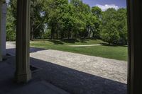 the view of a large open grassy park area from between two pillars with trees in background