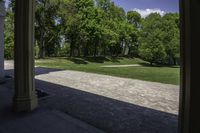 the view of a large open grassy park area from between two pillars with trees in background