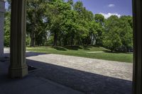 the view of a large open grassy park area from between two pillars with trees in background