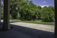 the view of a large open grassy park area from between two pillars with trees in background