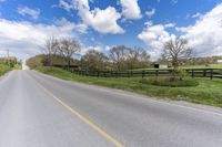 the empty road next to an pasture with a horse and a house on the right