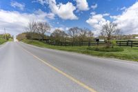 the empty road next to an pasture with a horse and a house on the right