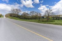 the empty road next to an pasture with a horse and a house on the right