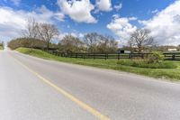 the empty road next to an pasture with a horse and a house on the right