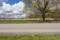 an empty road passing through some fields and trees in the distance, near the side of the road