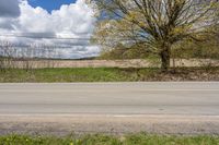 an empty road passing through some fields and trees in the distance, near the side of the road